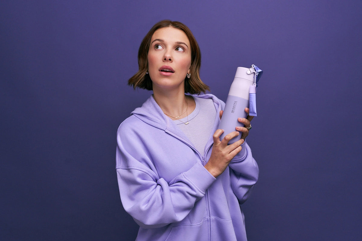 Millie Bobby Brown is holding the florence by mills x BRITA LARQ bottle on purple background.