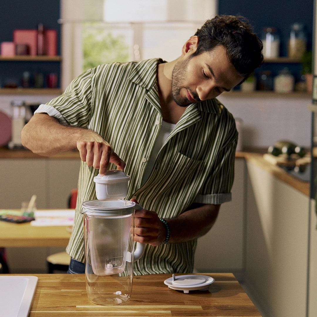 A man inserting MAXTRA filter cartridge in grey BRITA glass jug.
